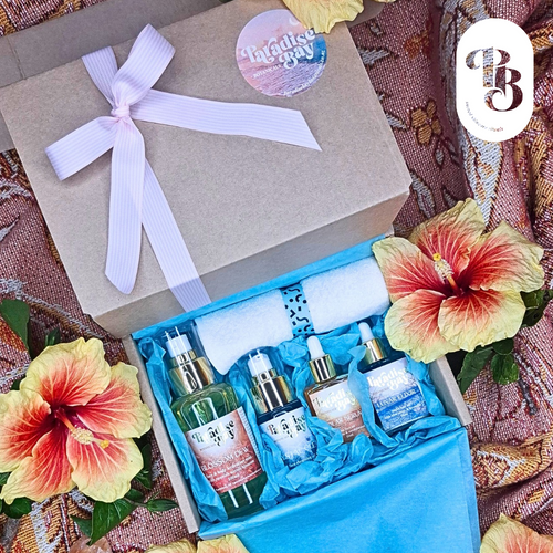 Open gift box with skincare products and tropical flowers on a patterned fabric background